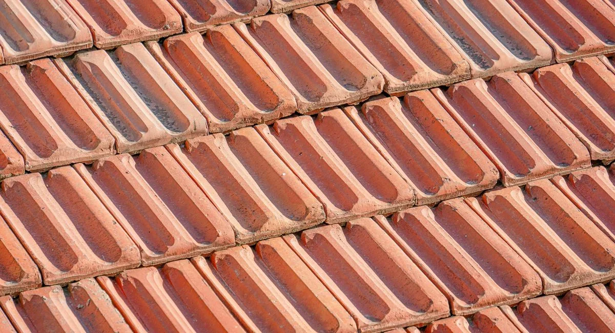 Couvreur installant un faîtage sur toiture avec tuiles rouges, ciel gris