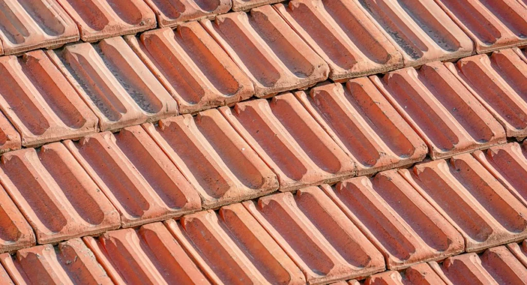 Couvreur installant un faîtage sur toiture avec tuiles rouges, ciel gris